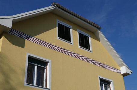 Painted stripe that looks like red “greater than“ signs near roof of building.