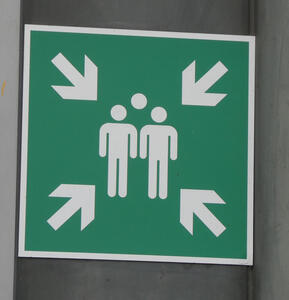 Green sign with icon of three people. Arrows point inwards from the four corners.