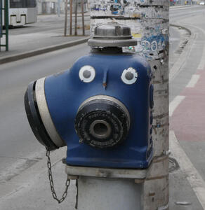 Blue hydrant with stickers that make it look as if the hydrant has eyes.