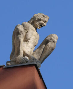 Sculpture of laughing man crouched on top of buidling.