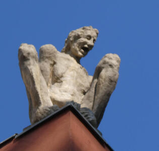 Sculpture of crouching, laughing man on top of building.