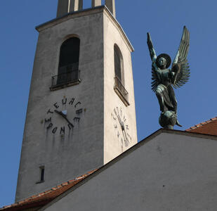 Church tower with angel sculpture on nearby roof of church