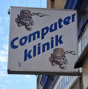 Sign for Computer Klinik. At upper left, an angry computer in bandages and with a crutch. At lower right, same computer, same condition, but smiling.