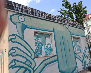 Abstract green bird; text at top of building: Wer nicht fragt bleibt dumm