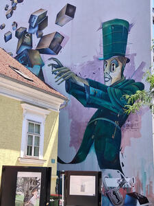 Mural of man in top hat making magical gesture at blocks floating in air.