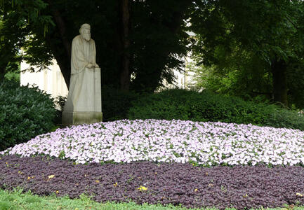 Sculpture of old bearded man behind a bed of purple and white flowers