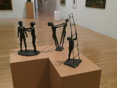 Woman reaching out to man; two people facing each other leaning back and holding hands; man holding a ladder upright