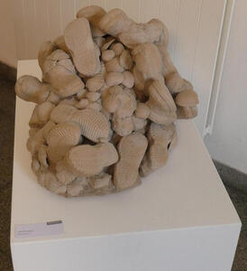 Seashells and shoes with soles upwards, piled on a person; only the person's head is visible