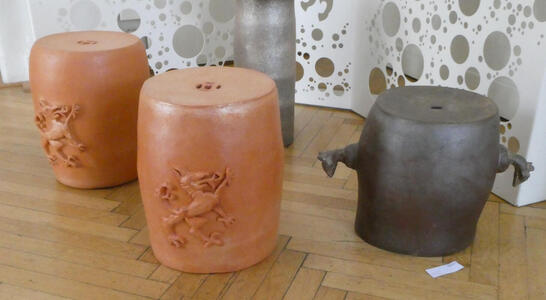 Three barrel-shaped artworks. Two are brown with the Steiermark seal on the; one is gray with short “arms” sticking out from the side.