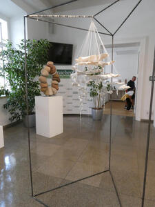 Foreground has  ceramic sculpture hanging from a wire framework, background has a circle composed of stones