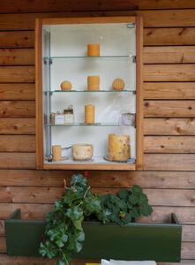 Cabinet with shelves of beeswax candles above a planter with a vine growing in it.
