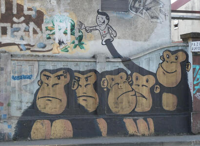 Four apes with glum expressions; the fifth ape is smiling. On his hand is a puppet of a human with a paintbrush in his hand. The puppet is wearing a shirt saying “I [heart symbol] Street Art”