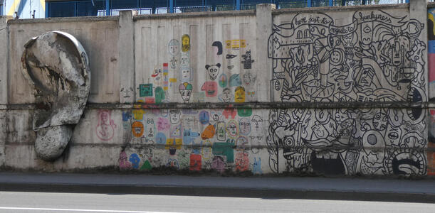 At left, a concrete ear protruding from the wall. In middle, people’s faces in various colors. At right, a somewhat abstract design in black and white with a banner “here just to regulate funkyness”