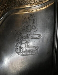Engraving of knight on his knees; it is on the shoulder of a suit of armor