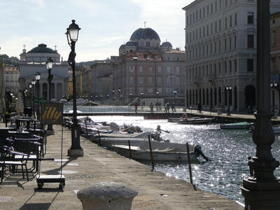The Trieste grand canal. A domed building is in the background. Sunlight reflects off the water.