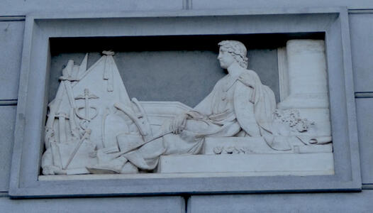 Carving of a man, reclining. Near him is an array of tools.
