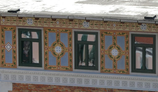 Building with rectangles painted between windows to look like window frames with floral designs, a circular center, and blue background