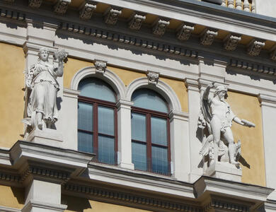 Statues flanking a window on an upper floor of a yellow building