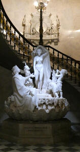 Statue of a woman holding a cloth above her head. she is surrounded by young children and a person with a crown