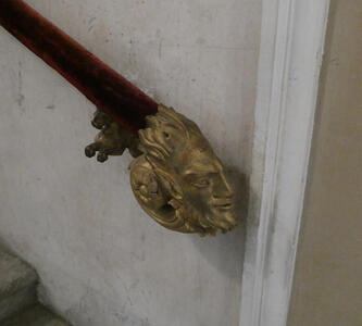 Gold-colored satyr’s head forming the end of a staircase railing