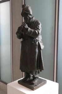 Bronze statue of man with hands folded in prayer, head downwards