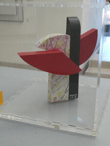 Abstract stone sculpture in red arcs with black and white columns. The white portion has pastel colors on it.