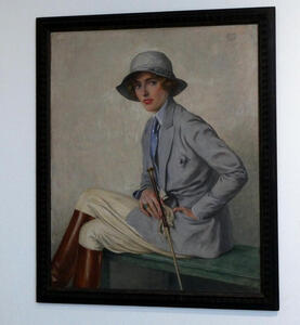 Portrait of horsewoman in jodhpurs and riding boots, with a riding crop in her hand.