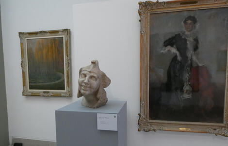 Stone bust of a Jester. It is between two oil paintings, one of trees and the other of a woman in a long frilly dress