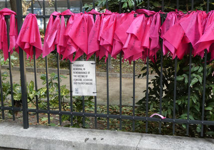 Pink cloths hanging from fence. Text on placard: Permanent memorial in remembrance of the victims of femicide, lesbicide, and transfemicide