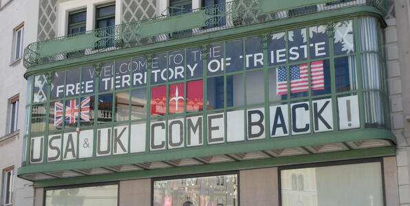 Sign in upper floor windows of a building: Welcome to the Free Territory of Trieste / USA & UK Come Back!