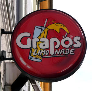 Sign for Grapos Limonade; in background, a glass with a straw and liquid splashing over the top.