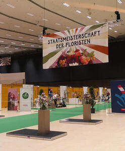 Sign: Staatsmeisterschaft der Floristen hanging above some flower arrangements