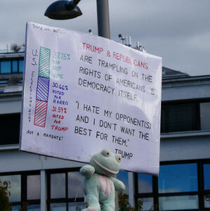 Sign: Trump & Republicans are trampling on the rights of Americans and democracy itself. ”I hate my opponent(s) and I don’t want the best for them.” -- Trump. A plush frog is attached to the bottom of the sign.