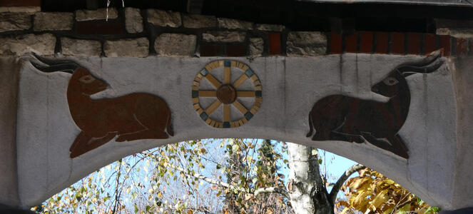 Archway decorated with two long-horned antelope-type creatures in repose; between them a prayer wheel mosaic.