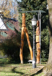 At left, wood statue with frowning person who has two very long legs. At right, a totem pole-like wooden sculpture with a chess knight’s horse head