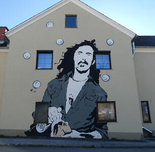 Wall art of a long-haired man with moustache and goatee smoking a cigarette. He is wearing a gray shirt open to reveal a white t-shirt.