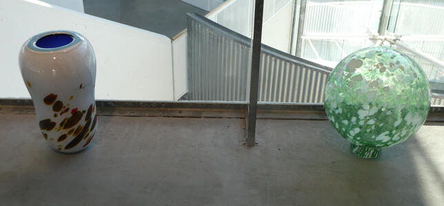 At left, a white urn with brown spots and blue interior. At right, a translucent green sphere with white highlights