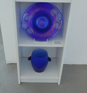 At top, cobalt blue dish with holes around edge; below a cobalt blue vase with stubby handles