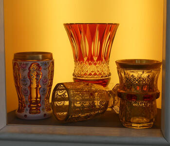 Four drinking glasses with ornate decoration. The one in the back is red with cut-glass design near the base.