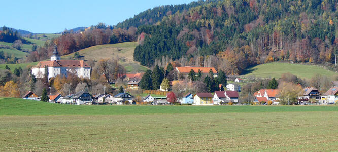 Field in foreground, small village with church in midground, forested hills in background.