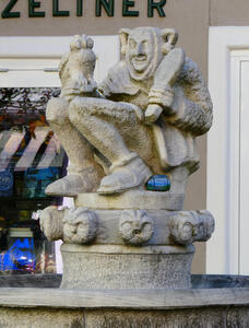 Statue of Till Eulenspiegel, seated, holding an owl and a mirror. At the base of the statue are owl heads.