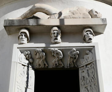 On top, a slab with a man lying on his back. The slab is supported by the heads of three men wearing medieval hats. Below them, a doorway showing people supporting one another.