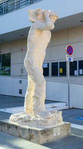 Sculpture of worker in hard hat, carrying a large power tool on his shoulder.