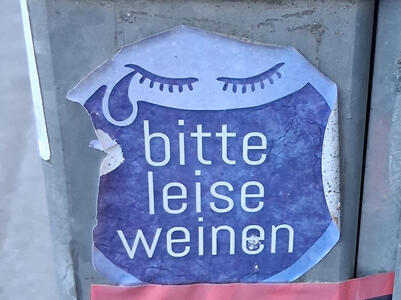 Large open mouth above a pair of eyelashes. One has a tear dropping from it. Text: bitte leise weinen