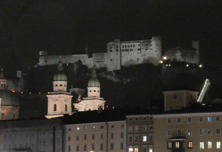 Nighttime view of city; two church domes in foreground, fortress on hill in background.