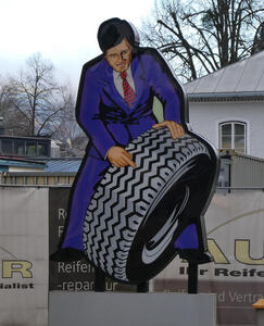 A cutout of man in suit pointing to tire.