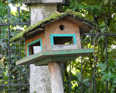 Wooden birdhouse with door frame in green, on a dark green base