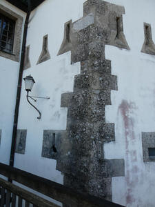 White wall with funnel-shaped window openings and staggered gray blocks at corner