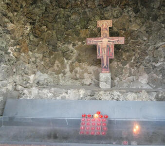 Stone niche with painted crucifix and votive candles in foreground