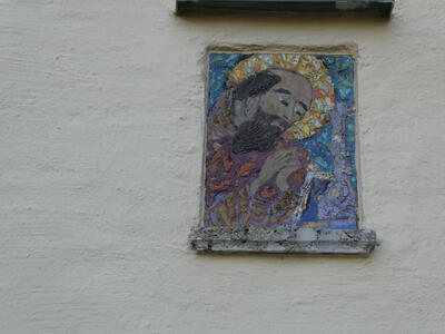 Painting of bald, bearded monk praying in front of a crucifix. The monk has a halo behind his head.